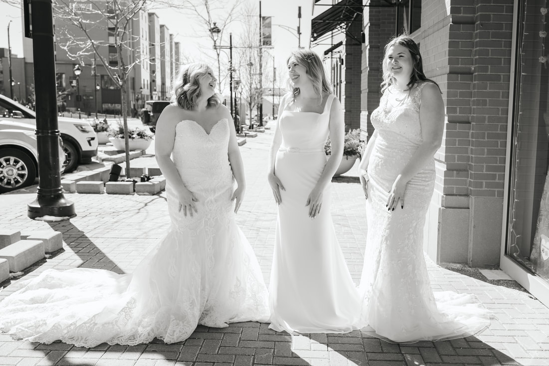 Three young women laughing in designer wedding dresses on sidewalk
